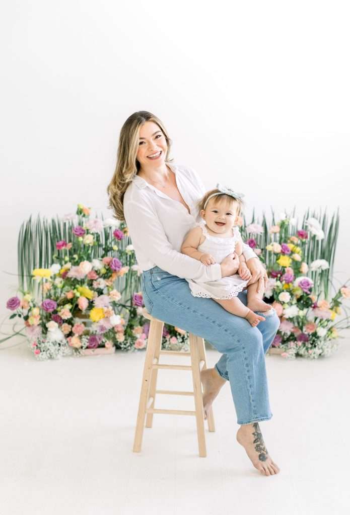 mom holding baby in front of floral installation 