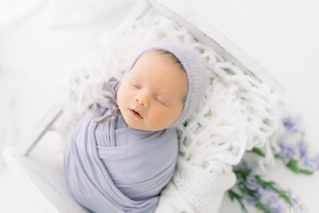Newborn baby girl sleeping in a rustic prop basket with soft floral accents, photographed by a Wesley Chapel newborn photographer.