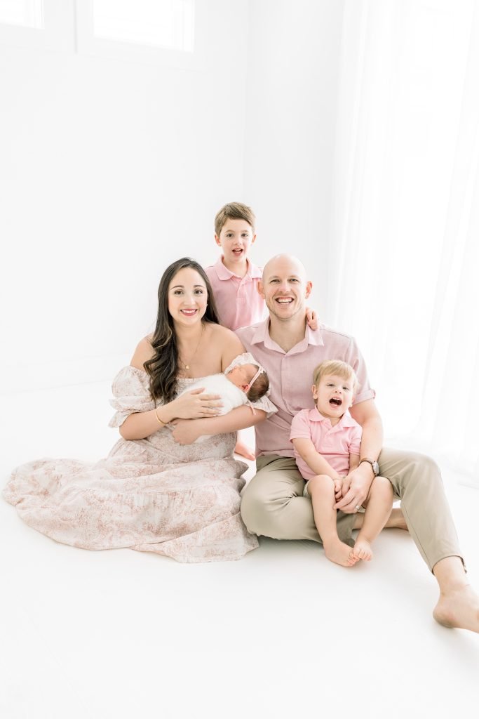 Professional studio portrait of a mother and father with their three children, including a newborn baby swaddled in white.