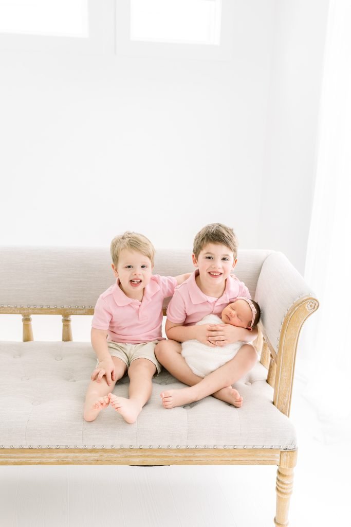 Two young brothers smiling and posing with their new baby sister during a newborn session in Wesley Chapel.